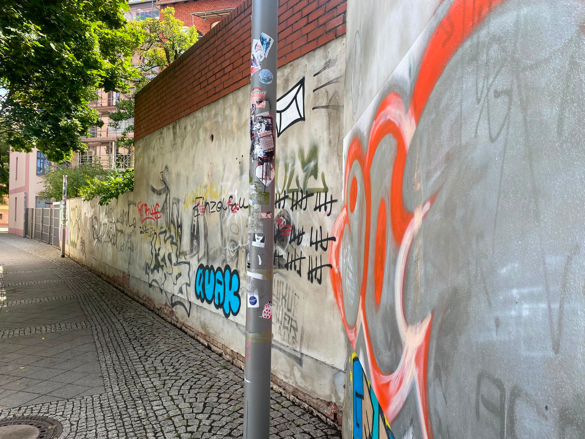 Betonmauer mit Graffiti, Aufklebern und Plakatresten an einem Laternenmast