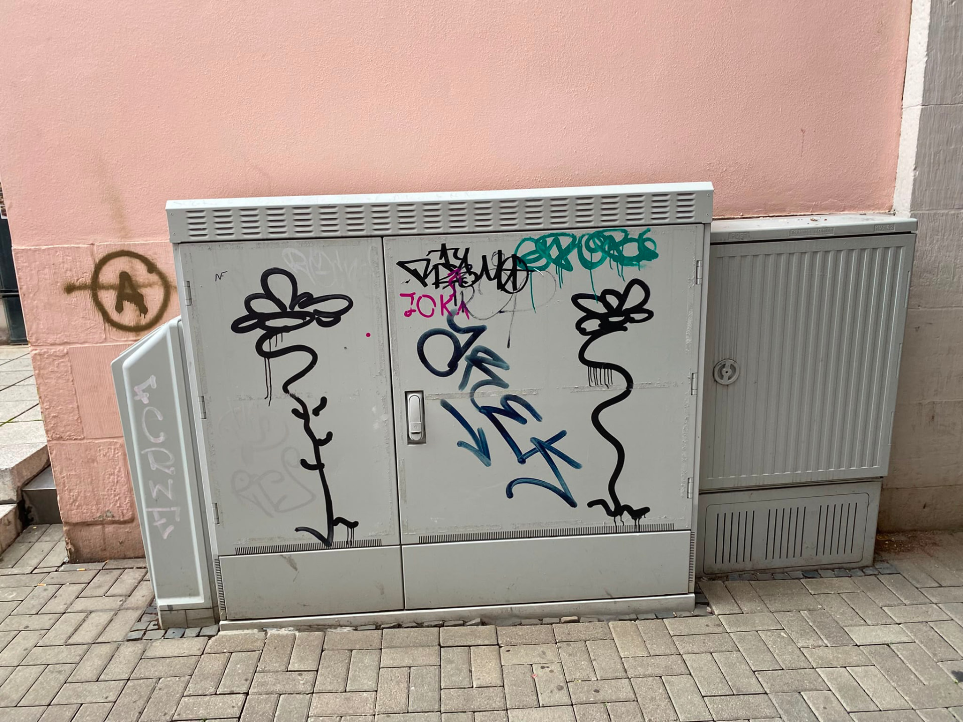 Grauer Verteilerkasten mit schwarzen und farbigen Tags vor rosa Wand