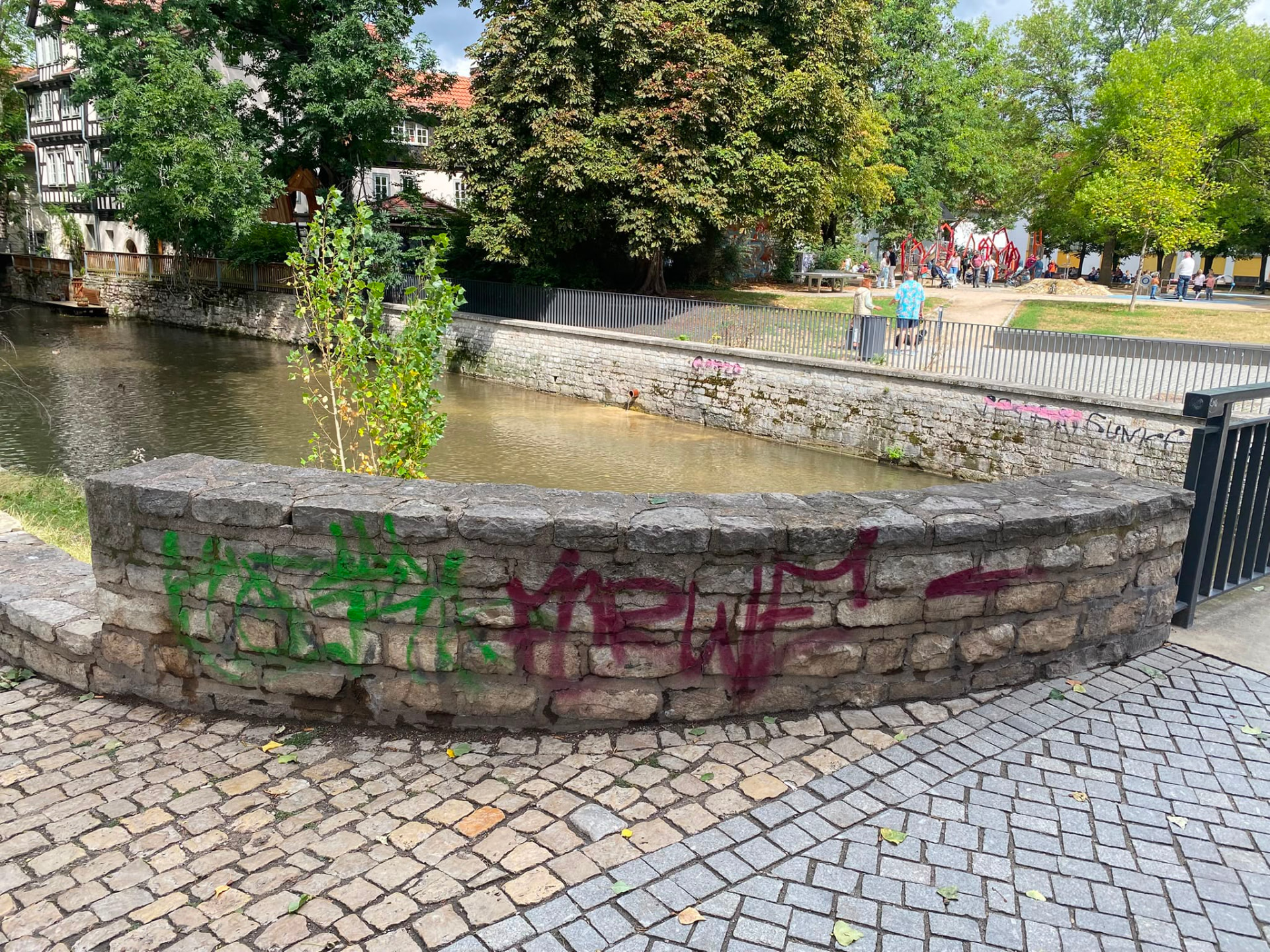 Historische Bruchsteinmauer an einem Fluss mit grünen und pinken Tags