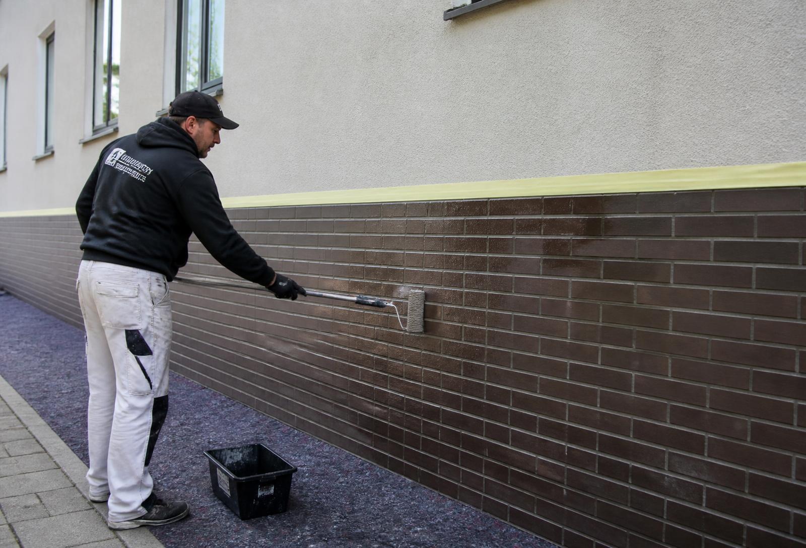Handwerker trägt eine transparente Anti-Graffiti-Beschichtung auf einen Klinkersockel auf