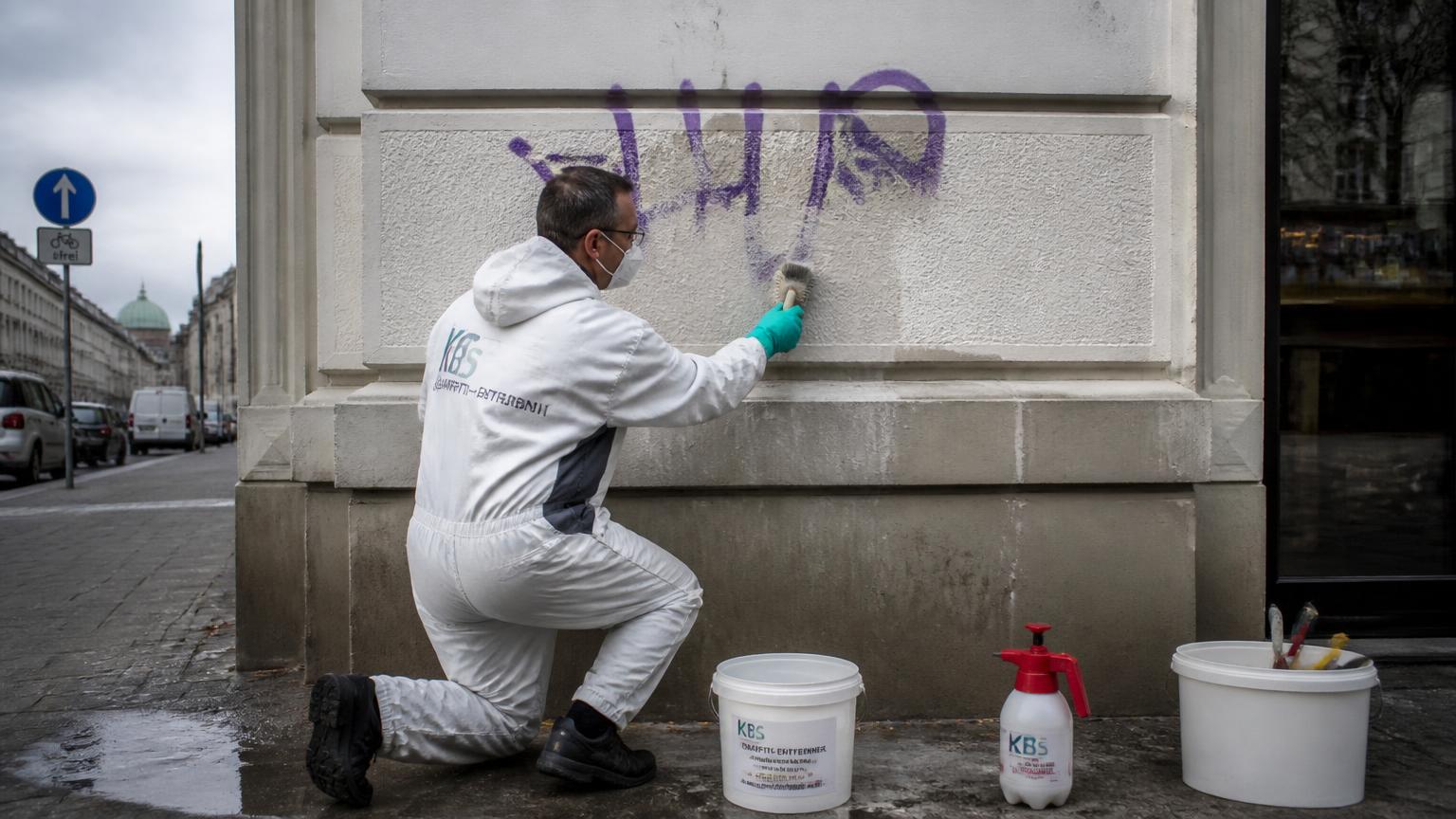 Fachkraft trägt Graffiti-Entferner mit einer Bürste auf eine Putzfassade auf