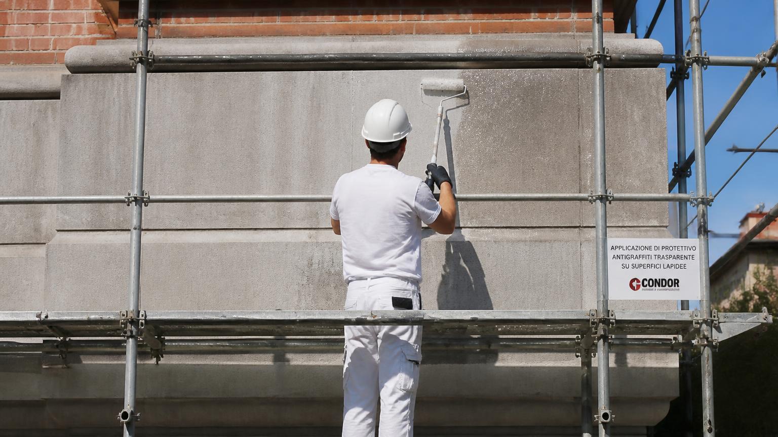 Handwerker rollt transparente Anti-Graffiti-Beschichtung auf eine Betonwand