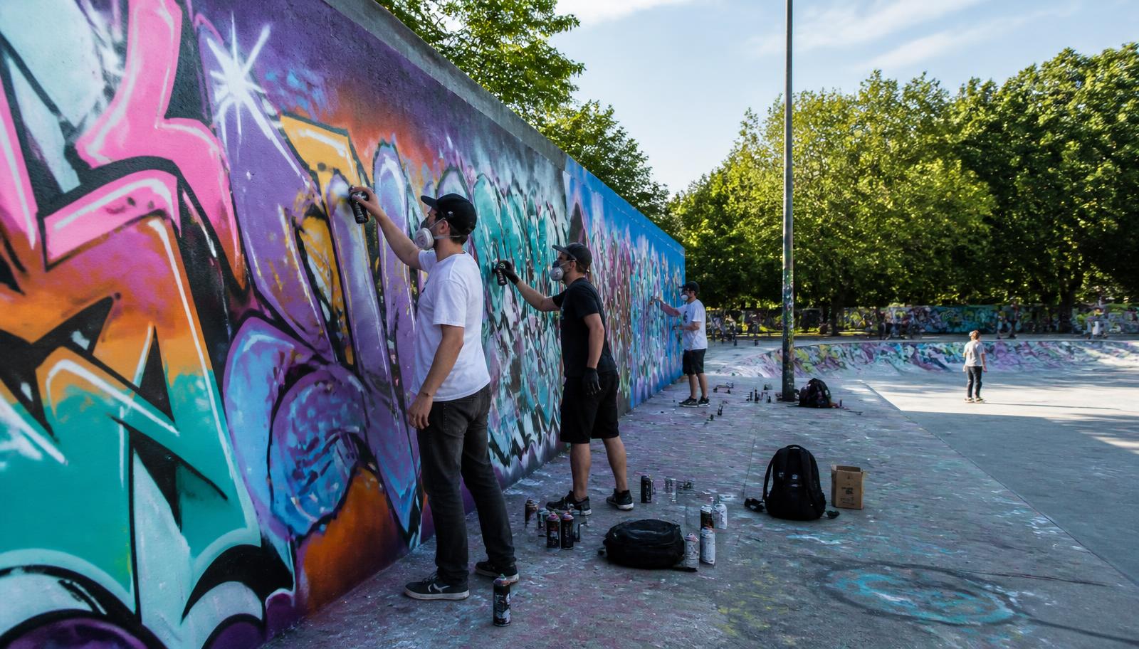 Junge Künstlerinnen und Künstler sprühen an einer legalen Graffiti-Wand an einem Skatepark